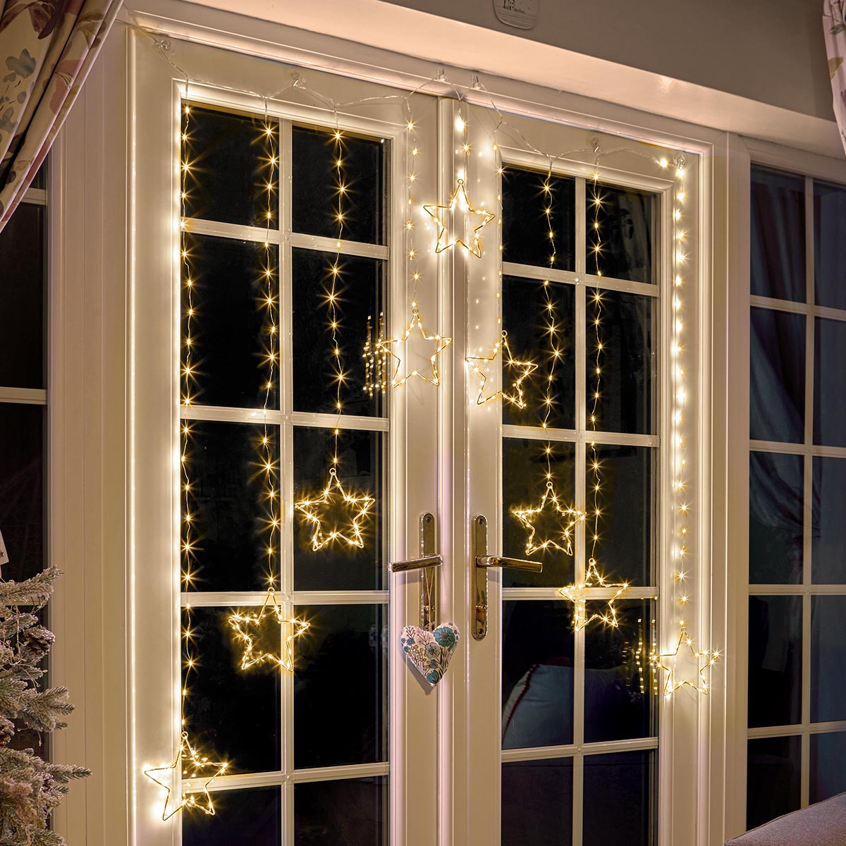 Warm white LED star curtain lights with hanging star-shaped bulbs displayed on a set of double French doors at night Christmas