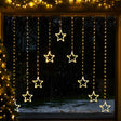 Warm white LED curtain string lights shaped like stars, hanging vertically in multiple strands across a christmas window during a snowy night scene.