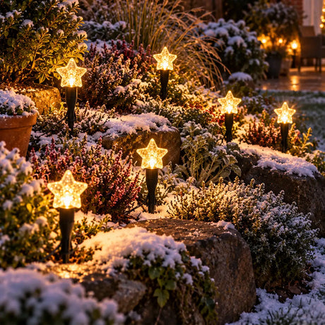 Six star-shaped solar garden lights with warm glowing bulbs are arranged on snowy stone steps in a landscaped garden at night.