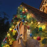 Outdoor Christmas garland wrapped around a wooden house corner at night, decorated with multicolored reflective ornaments, warm white string lights, and a white goat head wall decor.