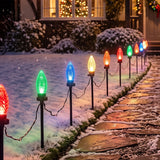 Outdoor Christmas stake lights on a snowy stone path, casting colorful light beams in red, green, blue, orange, and yellow at night.