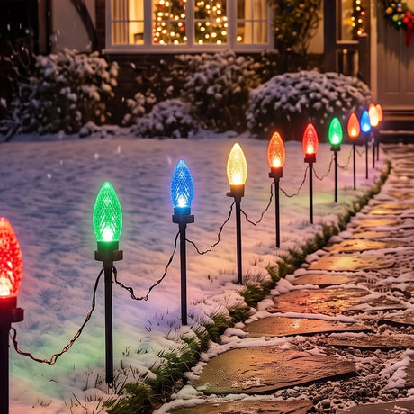 Outdoor Christmas stake lights on a snowy stone path, casting colorful light beams in red, green, blue, orange, and yellow at night.